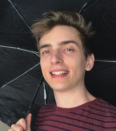 a young man holding an umbrella in his hand and smiling at the camera while wearing a striped shirt