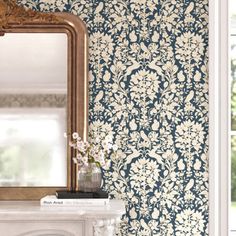 an ornate wallpapered room with a mirror and vase on the fireplace mantel