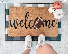 a person standing in front of a welcome mat with a football and pumpkins on it