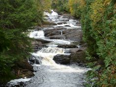 a river running through a forest filled with lots of rocks and water flowing down it's sides