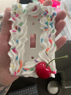 a hand holding a white light switch plate with sprinkles and a cherry