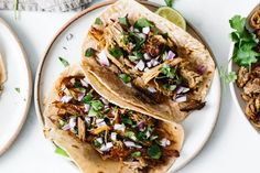 three tacos with meat, onions and cilantro on plates