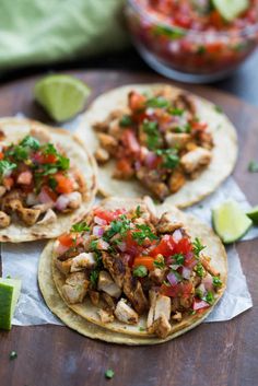 three tacos with chicken, tomatoes and cilantro on paper next to lime wedges