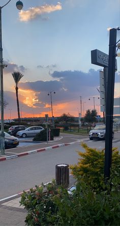 the sun is setting over a parking lot with cars parked on the side of the road