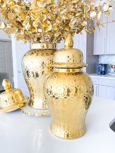 two gold vases sitting on top of a white counter next to a potted plant