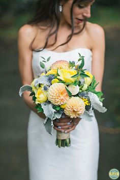 a woman in a white dress holding a bouquet of yellow and gray flowers on her wedding day