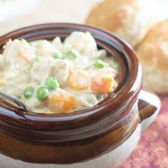 a close up of a bowl of food on a table with bread in the background