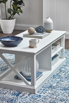 a white coffee table with blue and white decor on it in front of a plant