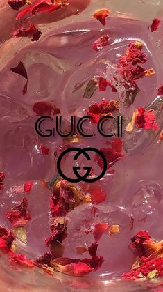 a glass bowl filled with pink liquid and rose petals on top of it, next to a gucci logo