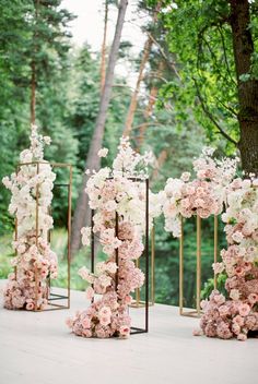 pink and white flowers are arranged on gold stands in the middle of an outdoor ceremony