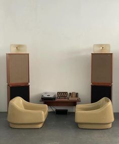 two beige chairs sitting next to each other in front of a table with speakers on it