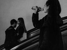 a woman drinking from a bottle while standing on an escalator next to another man