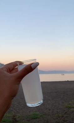 a hand holding a glass with water in it on the beach at sunset or dawn