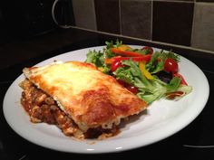 a white plate topped with lasagna next to a salad on top of a counter