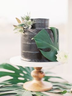 a black cake with green leaves and flowers on top