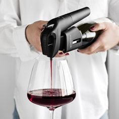 a person pouring red wine into a glass with a bottle in the other hand,