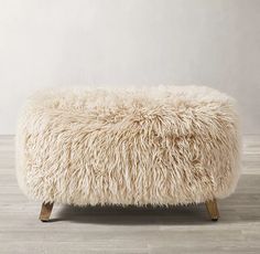 a sheepskin footstool on wooden legs in a room with white walls and wood flooring