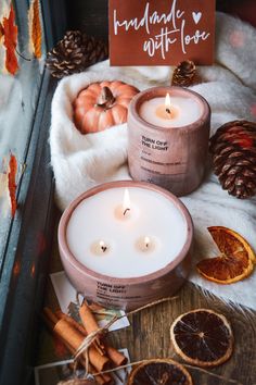 two candles sitting on top of a wooden table next to oranges and pine cones