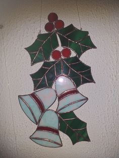 a stained glass christmas ornament hanging from the ceiling with holly leaves and bells