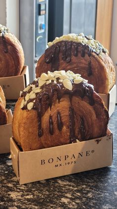 three breads with chocolate drizzled on them sitting in a cardboard box