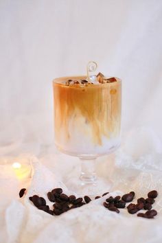 an iced drink with coffee beans on the table next to it and a lit candle