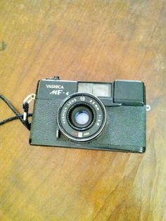 an old fashioned camera sitting on top of a wooden table next to a black cord