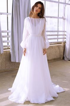 a woman wearing a white dress standing in front of a window