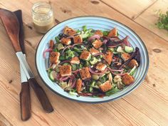 a salad with croutons and onions in a blue bowl on a wooden table