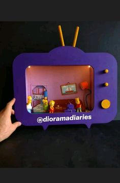 a hand holding up a purple tv with the simpsons on it