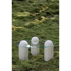 three white balls sitting on top of a glass table in the middle of green grass