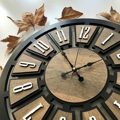 a wooden clock with roman numerals and leaves