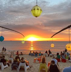 people are sitting on the beach at sunset with lanterns hanging from the ceiling above them