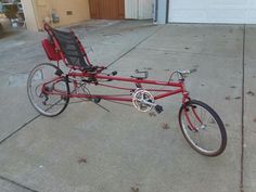 a red bicycle parked in front of a garage with a black seat on the back