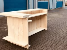 a wooden desk sitting on top of a brick floor next to blue doors in a parking lot