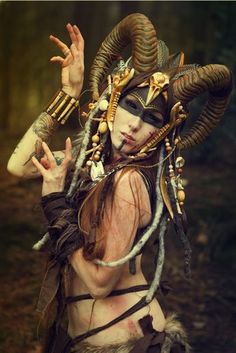 a woman with horns and makeup is posing in the woods wearing an elaborate headdress