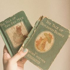 two children's books are being held up in front of the camera with their hands