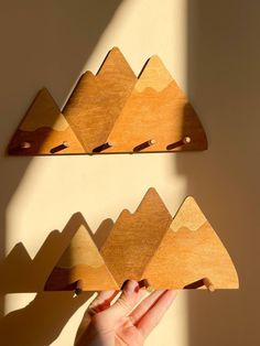 two wooden mountains are hanging on the wall and someone is holding their hand up to them