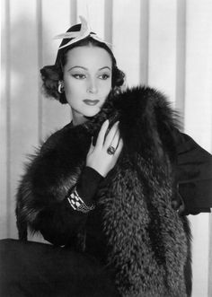 a black and white photo of a woman wearing a fur coat with a bow on her head