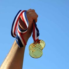 a man holding up two medals in his hand with a blue sky behind him on a sunny day