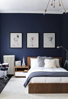 a bedroom with dark blue walls and white carpeted flooring, two paintings on the wall