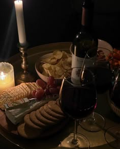 a glass of wine and some crackers on a table with a lit candle in the background