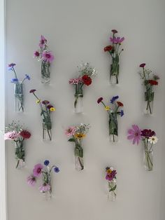 several vases filled with different types of flowers on a white wall next to a window