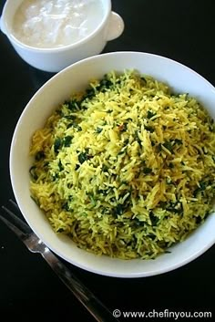 a white bowl filled with yellow rice next to a cup of yogurt on a black table