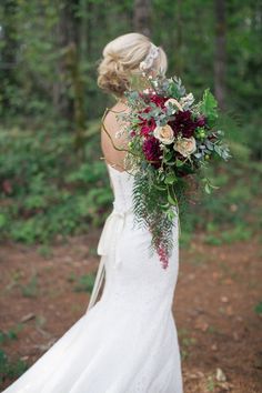 a woman in a white dress holding a bouquet of flowers and greenery on her wedding day