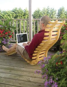 an older man sitting in a wooden chair on a porch working on his laptop computer