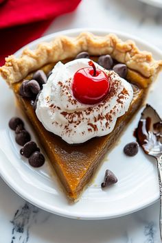 a slice of pumpkin pie with whipped cream and chocolate chips on a white plate next to a fork