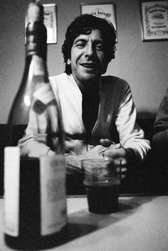 a black and white photo of a man sitting at a table next to a wine bottle