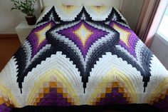 a bed covered in a colorful quilt next to a window with potted plant on it