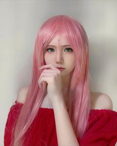 a woman with long pink hair and blue eyes posing in front of a white wall