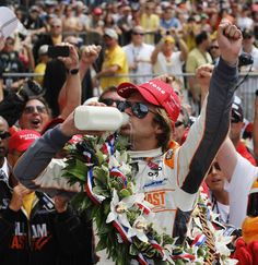 a man drinking from a bottle in front of a large group of people at a race